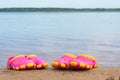 Children`s pink clogs stand on a sandy beach near the water. Royalty Free Stock Photo