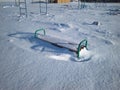 Children`s Playground with swings covered with snow in winter a bench in a snowdrift Royalty Free Stock Photo