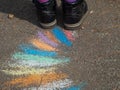 Children`s Rainbow chalk drawing art on asphalt painted with colored crayons and girl`s feet in boots on colorful road Royalty Free Stock Photo