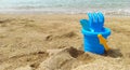 a children's sand bucket with a children's rake and a shovel in focus stands on the sand on the seashore Royalty Free Stock Photo