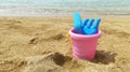 a children's sand bucket with a children's rake and a shovel in focus stands on the sand on the seashore Royalty Free Stock Photo