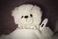 Children`s soft toy Teddy bear measures the temperature with an electronic thermometer lying in bed. Children s hospital. Concept Royalty Free Stock Photo
