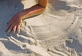 Children`s tanned hand on the beach smoothes the beach sand on the breath