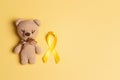 Children`s toy with a Childhood Cancer Awareness Yellow Ribbon on yellow background