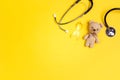 Children`s toy with a Childhood Cancer Awareness Yellow Ribbon and stethoscope on yellow background with copy space