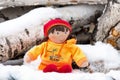 Children`s toy doll in the snow on logs outside a winter country cottage