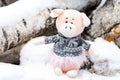 Children`s toy pig in the snow on birch logs outside the winter cottage