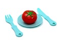 Children`s toy plastic tableware: plate with tomato, fork and knife. Serving set Royalty Free Stock Photo