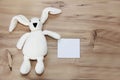 Children`s toy soft white plush rabbit with long ears holds a greeting card on a wooden background Royalty Free Stock Photo