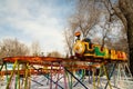 A children`s train rides on high rails over snowdrifts among trees in a city amusement park Royalty Free Stock Photo