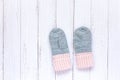 Children`s winter accessories, warm knitted mittens - gray with pink hearts on white wooden background.