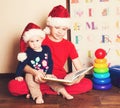 Children in Santa hats reading a Christmas book. Big brother reading to his little baby sister in the nursery. Royalty Free Stock Photo