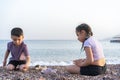 Children show each other sea pebbles. Two kids sitting on sea beach in summer day. Royalty Free Stock Photo