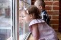 Children or siblings concept. Little girl and boy sitting at window and watching outside