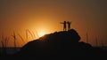 Children silhouettes against the sunset. Boys in hats with brims stand on a rock. The stone lies on the shore of the sea