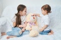 Two children, sisters play on a white sofa in white t-shirts and blue jeans. Soft plush Bunny