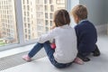children sit on floor by window and admire view during quarantine. little blond boy and girl with pigtails looking at something Royalty Free Stock Photo