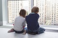 children sit on floor by window and admire view during quarantine. little blond boy and girl with pigtails looking at something Royalty Free Stock Photo