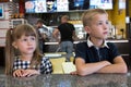 Children sitting in fast food restaurant behind empty table waiting for food Royalty Free Stock Photo