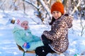 Children sitting on sledge in the winter forest and playing, bright sunlight and shadows on the snow, beautiful nature Royalty Free Stock Photo