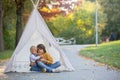 Children, sitting in a tent teepee, holding teddy bear toy with