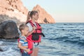 Children stand on seashore in red life vests and stormy sea. Safety of people on water. Kids wear life jackets ready for boat trip Royalty Free Stock Photo