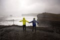 Children, standing at the edge of the ocean on heavy rain day near Dyrholaey, watching the huge waves, Iceland wintertime Royalty Free Stock Photo