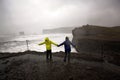 Children, standing at the edge of the ocean on a heavy rain day near Dyrholaey, watching the huge waves, Iceland