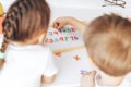 Children study the letters on the magnet and lay them out in a row on the board while sitting at the table Royalty Free Stock Photo