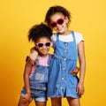 Children, sunglasses and happy sisters in studio hug for love, care and support of family on yellow background. Cute Royalty Free Stock Photo