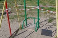 Children swing with wooden seat with metal green back with welded iron pipes racks. Swing is tied with red and white signal tape