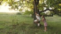 Children swinging on swing on an oak branch in sun. Dreams of flying. concept of happy childhood. Beautiful girls are