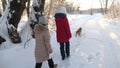 Children teens travel in winter in the park with a dog. two girls and dog and dog walk along path in winter park Royalty Free Stock Photo