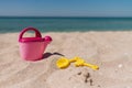 Children toys on a sand beach with blue background. A pink toy watering can with yellow shovel and rake. Royalty Free Stock Photo