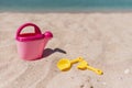 Children toys on a sand beach with blue ocean background. A pink toy watering can with yellow shovel and rake. Vacation with child Royalty Free Stock Photo