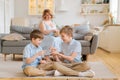 Children two brothers play together on floor, while young mother sits at home