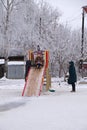 Children two girls ride in the winter with a wooden slide under the control of adults