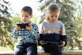 Children use gadgets while sitting in the park outdoors, games on smartphone and tablet Royalty Free Stock Photo