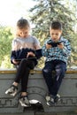 Children use gadgets while sitting in the park outdoors, games on smartphone and tablet Royalty Free Stock Photo