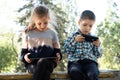 Children use gadgets while sitting in the park outdoors, games on smartphone and tablet Royalty Free Stock Photo