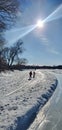 Children walking on a path on a snowy day over a frozen lake in the sunshine.