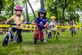 Children wearing protective helmets ride tricycles through a park on a sunny day Royalty Free Stock Photo