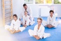Children in white kimono sits in butterfly pose and practices stretching in sport gym