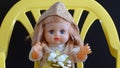 podarkom na kolenyakh.On a yellow chair sits a baby doll with blue eyes, blond hair with a gift on its knees.