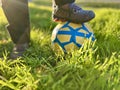 Children& x27;s foot of the winner in an old sports shoes sneaker stands on a soccer ball against a background of grass Royalty Free Stock Photo