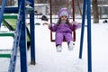 children's playground in winter. A little girl goes for a drive on a swing during a snowfall. Royalty Free Stock Photo