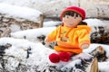 Children's toy doll in the snow on logs outside a winter country cottage