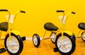 Children yellow bicycles stand in a row against a yellow wall in a kindergarten