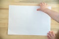 Childrens hand holding blank white paper sheet on wooden background. Copy space. Template. Mockup