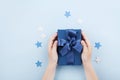 Childrens hands holding a gift or present box decorated confetti stars on blue table top view.